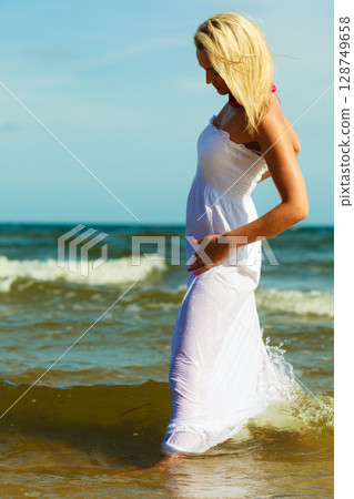 Blonde woman wearing dress walking in water 128749658