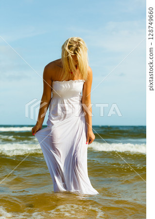 Blonde woman wearing dress walking in water Blonde woman wearing dress walking in water 128749660