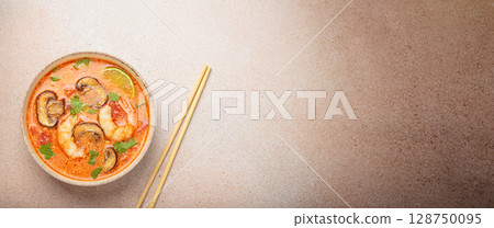 Tom yum soup with shrimp and mushrooms in bowl with chopsticks top view, traditional Thai soup Tom yum soup with shrimp and mushrooms in bowl with chopsticks top view, traditional Thai soup 128750095