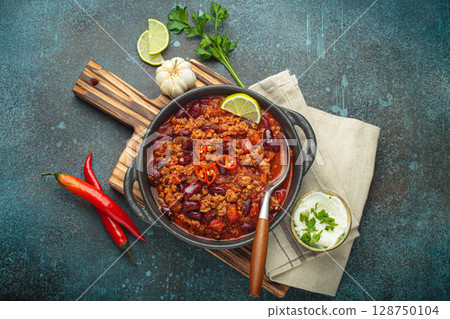 Mexican Chili con carne with minced meat, red beans, tomatoes, lime, and spices in a cast iron pot 128750104