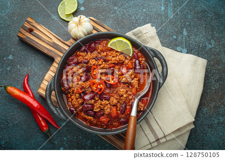 Mexican dish Chili con carne with lime, garlic and chili pepper on dark background top view 128750105