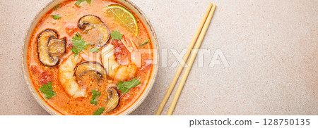 Tom yum soup with shrimp and mushrooms in bowl with chopsticks top view, traditional Thai soup, space for text Tom yum soup with shrimp and mushrooms in bowl with chopsticks top view, traditional Thai soup, space for text 128750135