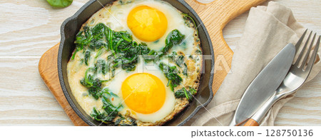 Healthy spinach omelette with two fried eggs in cast iron pan top view 128750136
