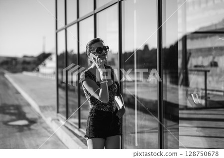 A girl with a long braided ponytail stands outside a glass building, holding her phone to her ear 128750678