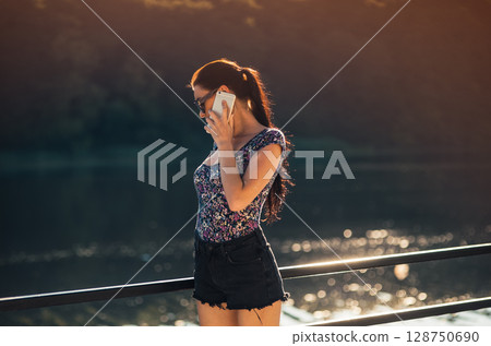The girl in stylish sunglasses with a braided ponytail stands by the lake The girl in stylish sunglasses with a braided ponytail stands by the lake 128750690