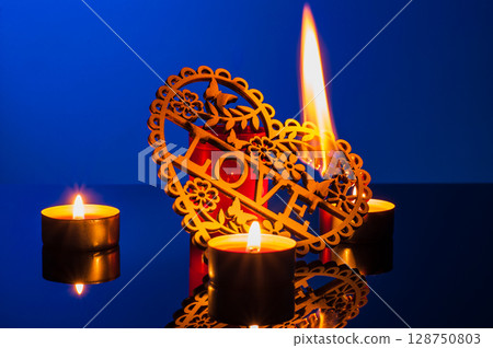Romantic candles flicker in the photo, surrounding a decorative wooden heart Romantic candles flicker in the photo, surrounding a decorative wooden heart 128750803