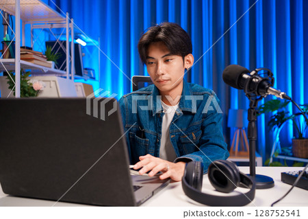 Podcast host preparing live recording in professional studio with microphone and laptop Podcast host preparing live recording in professional studio with microphone and laptop 128752541