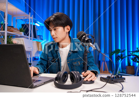 Young man working on podcast production with microphone and laptop in studio 128752544