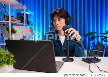 Young man working on podcast production with microphone and laptop in studio 128752567
