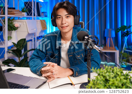Man podcaster influencer blogger smiling while broadcasting his live audio podcast in studio using headphones. Male radio host making podcast or interview. 128752623