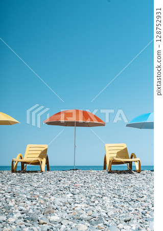 Colorful Beach Umbrellas and Sun Loungers on a Pebble Seaside 128752931