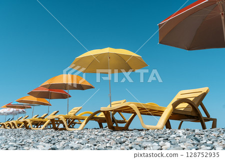Colorful Beach Umbrellas and Sun Loungers on a Pebble Seaside 128752935