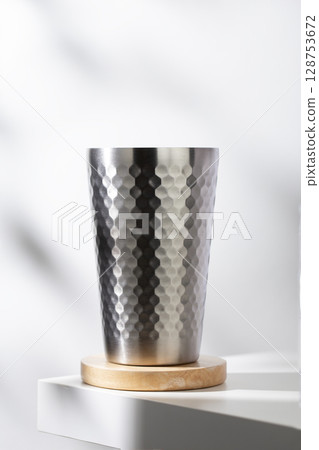 Chic stainless tumbler, dimpled texture, on a warm wooden coaster. Keeps drinks perfectly cold. Chic stainless tumbler, dimpled texture, on a warm wooden coaster. Keeps drinks perfectly cold. 128753672