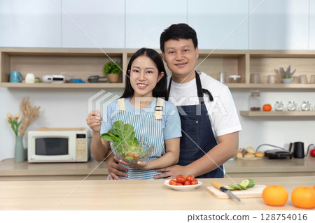 Happy Couple Preparing Salad Together in Bright Kitchen 128754016