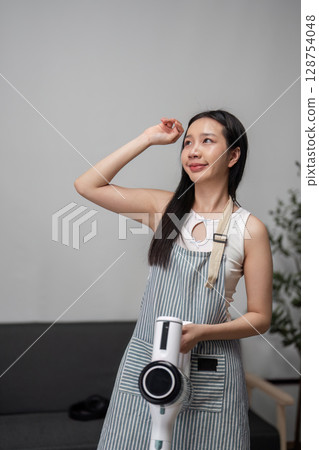 Young Woman Joyfully Cleaning Modern Home with Vacuum in Stylish Interior Setting Young Woman Joyfully Cleaning Modern Home with Vacuum in Stylish Interior Setting 128754048
