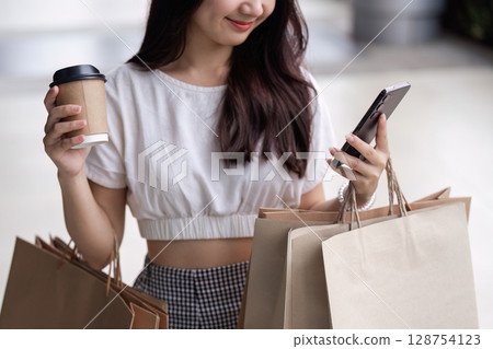 Young Woman Enjoys Black Friday Shopping Spree with Multiple Bags and Coffee in Hand Young Woman Enjoys Black Friday Shopping Spree with Multiple Bags and Coffee in Hand 128754123