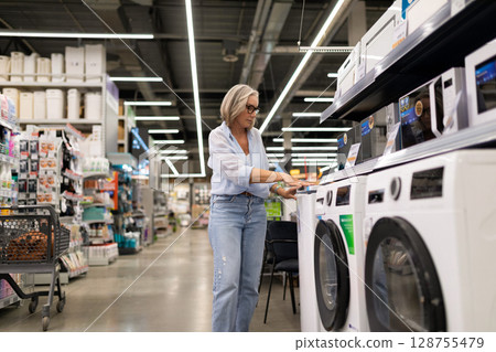 Woman selecting household items in a hypermarket, capturing real emotions and interactions while 128755479