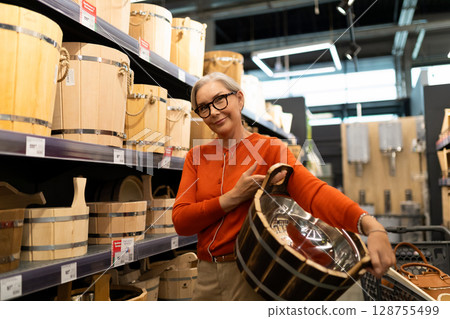 Middle-aged woman shopping in a home improvement store, exploring kitchenware and decor items Middle-aged woman shopping in a home improvement store, exploring kitchenware and decor items 128755499