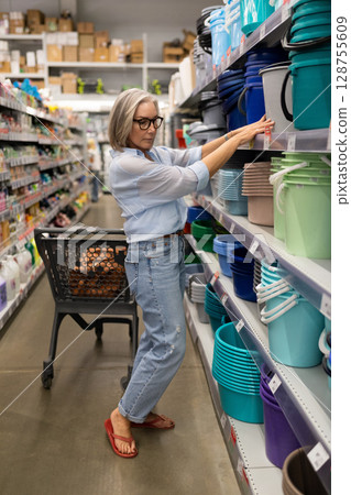 Woman shopping in a hypermarket while selecting colorful storage containers for home organization 128755609