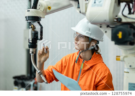 women echnician maintenance checking hardware robotic arm system of automation machine in factory. Service programming machinery welding robots in production at factory industry. women echnician maintenance checking hardware robotic arm system of automation machine in factory. Service programming machinery welding robots in production at factory industry. 128755974