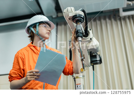 women echnician maintenance checking hardware robotic arm system of automation machine in factory. Service programming machinery welding robots in production at factory industry. women echnician maintenance checking hardware robotic arm system of automation machine in factory. Service programming machinery welding robots in production at factory industry. 128755975