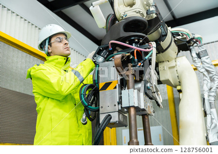 Repairman checking hardware robotic arm system of automation machine in factory. Service programming machinery welding robots in production at factory industry. Repairman checking hardware robotic arm system of automation machine in factory. Service programming machinery welding robots in production at factory industry. 128756001