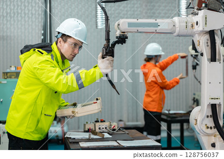 Robotic automatic technician man holding remote checking plan system of automation machine. Programming machinery welding robot in production at manufacturing industrial. Robotic automatic technician man holding remote checking plan system of automation machine. Programming machinery welding robot in production at manufacturing industrial. 128756037
