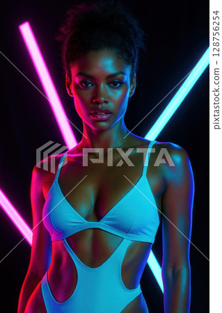 Portrait of Woman Illuminated by Neon Pink and Blue Light Tubes against Black 128756254
