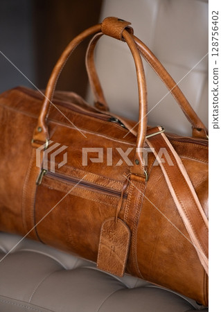 A vintage-style brown leather duffel bag rests on a cream-colore A vintage-style brown leather duffel bag rests on a cream-colore 128756402