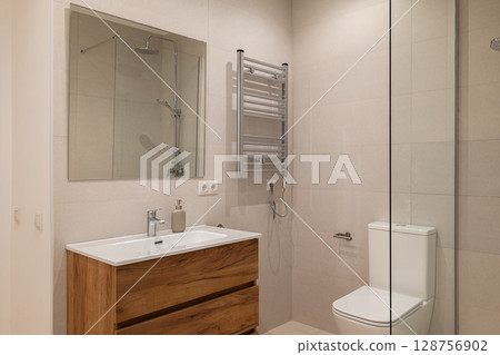 Bathroom with wood vanity, chrome towel warmer, glass shower and beige tiled walls 128756902