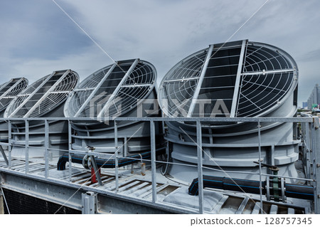 Cooling fans are installed on rooftop of large commercial building. Maintaining air circulation and temperature control. Tower air chiller HVAC. Cooling fans are installed on rooftop of large commercial building. Maintaining air circulation and temperature control. Tower air chiller HVAC. 128757345
