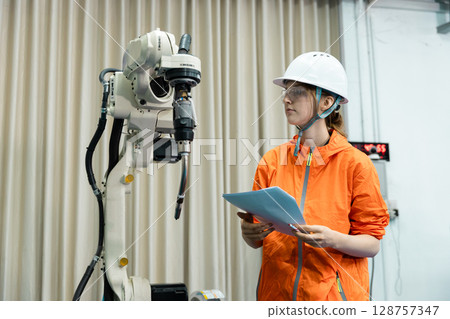 Robotic engineer women automatic mechanic with blueprint checking quality system of automation robot arms machine in factory. Service programming machinery welding robots in production at factory. Robotic engineer women automatic mechanic with blueprint checking quality system of automation robot arms machine in factory. Service programming machinery welding robots in production at factory. 128757347