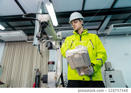 Robotic automatic technician man holding remote checking plan system of automation machine. Programming machinery welding robot in production at manufacturing industrial. 128757348