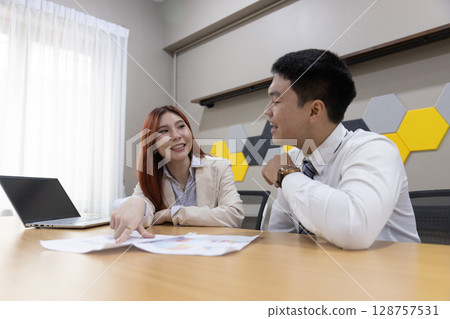 Colleagues collaborate over financial documents, pointing out key figures and charts in a contemporary office environment, enhancing teamwork and communication. 128757531
