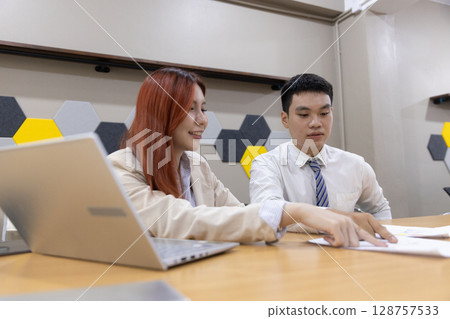 Colleagues collaborate over financial documents, pointing out key figures and charts in a contemporary office environment, enhancing teamwork and communication. 128757533