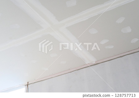 Interior building renovation progress showing new gypsum board ceiling with smooth edges ready for plastering. Electrical wire visible before final smooth finish applied to ceiling surface Interior building renovation progress showing new gypsum board ceiling with smooth edges ready for plastering. Electrical wire visible before final smooth finish applied to ceiling surface 128757713