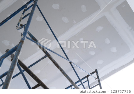 Scaffolding at construction site for house renovation. drywall ceiling shows progress during building and repair process for home improvement with new plasterboard Scaffolding at construction site for house renovation. drywall ceiling shows progress during building and repair process for home improvement with new plasterboard 128757736