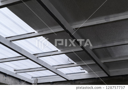 View looking up building roof structure displaying metal supports and translucent sheet panels. Composite sheet construction often uses layers including foam and pu for lightweight insulation View looking up building roof structure displaying metal supports and translucent sheet panels. Composite sheet construction often uses layers including foam and pu for lightweight insulation 128757737