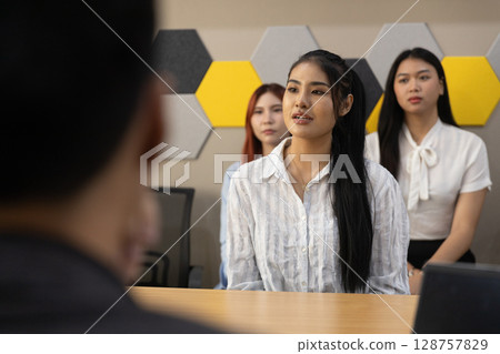 Sleek office with contemporary design, a young woman speaks confidently while presenting her thoughts. Two attentive colleagues listen closely, emphasizing teamwork and professional engagement. Sleek office with contemporary design, a young woman speaks confidently while presenting her thoughts. Two attentive colleagues listen closely, emphasizing teamwork and professional engagement. 128757829