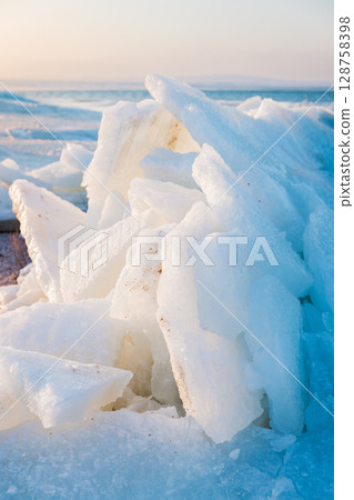 Frozen ocean shoreline with stacked ice slabs on sunset, winter landscape of broken crystalline layers. 128758398