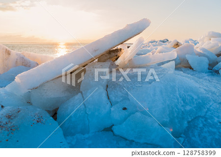 Close up of stacked ice slabs on a frozen coastline, glowing with golden light and deep blue shadows. Close up of stacked ice slabs on a frozen coastline, glowing with golden light and deep blue shadows. 128758399