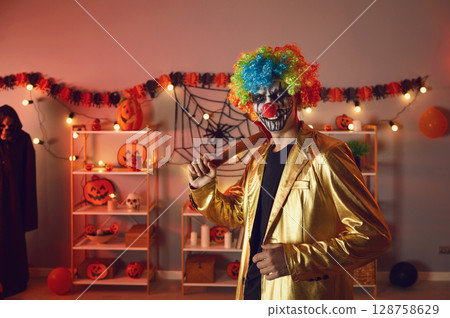 Portrait of adult man dressed up as creepy evil clown with axe at Halloween party 128758629
