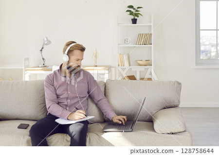 Young man in earphones work online on laptop at home 128758644