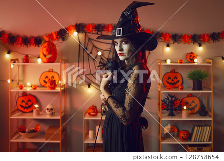 Portrait of mysterious and serious woman witch in room with Halloween decorations. 128758654