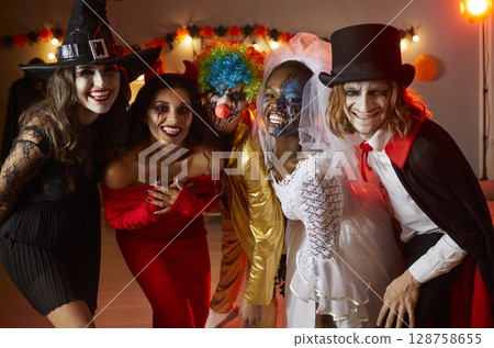 Group of happy friends dressed up in spooky Halloween costumes standing together and smiling 128758655