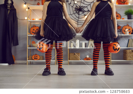 Two kids dressed up for Halloween go trick or treating with orange pumpkin baskets Two kids dressed up for Halloween go trick or treating with orange pumpkin baskets 128758683