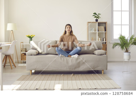 Calm woman practice yoga meditate on couch 128758684