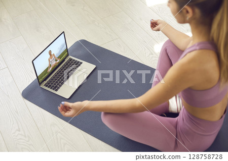 Woman watching video lesson on meditation or practicing yoga with online teacher 128758728