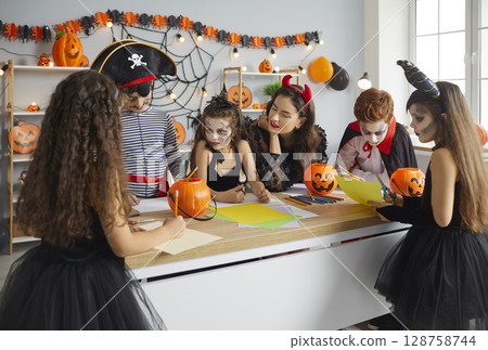 Group of children together with woman prepares handmade Halloween decorations from paper. Group of children together with woman prepares handmade Halloween decorations from paper. 128758744