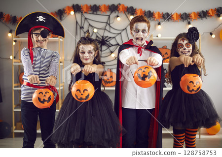 Four children in carnival costumes and with spooky make-up extend their buckets pumpkins to camera. 128758753